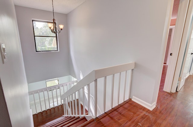 staircase with wood-type flooring, a textured ceiling, and a chandelier