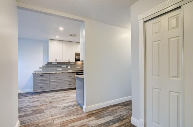 kitchen with decorative backsplash, gray cabinets, white cabinets, light hardwood / wood-style floors, and stainless steel range with electric cooktop