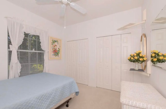 bedroom with light carpet, ceiling fan, and two closets