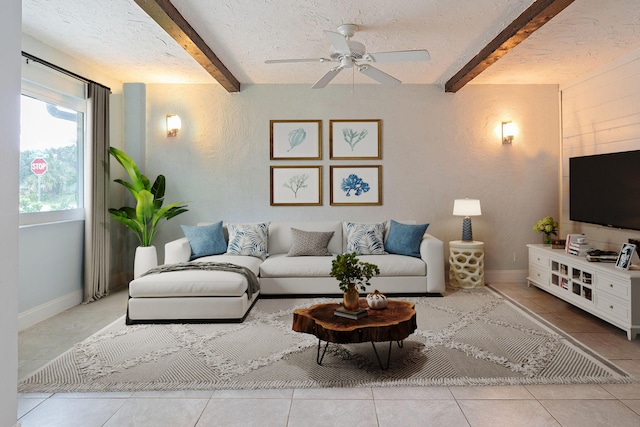 living room featuring beamed ceiling, ceiling fan, light tile patterned floors, and a textured ceiling