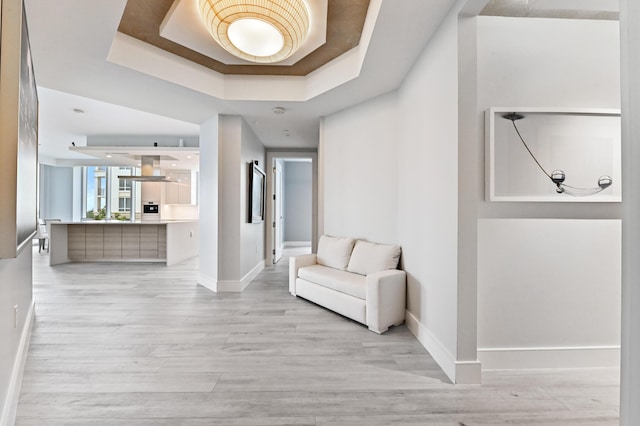 hallway featuring a raised ceiling, light wood-style flooring, and baseboards