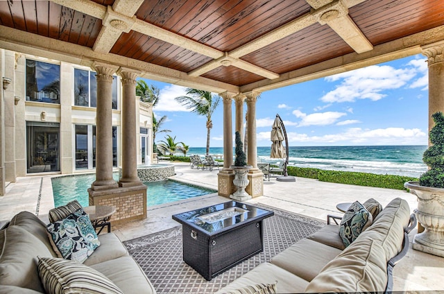 view of patio / terrace with a view of the beach, a water view, and an outdoor living space with a fire pit