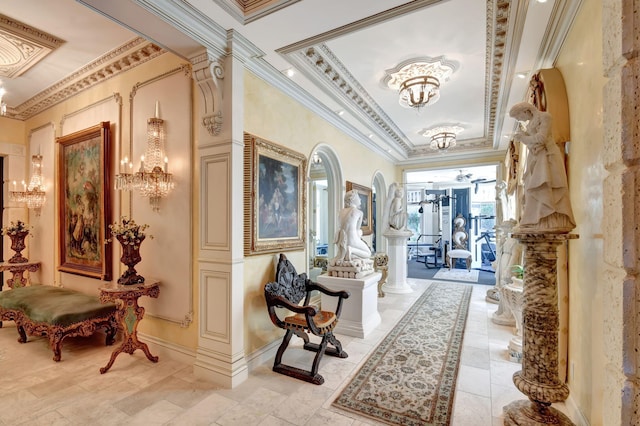 hall featuring crown molding, a tray ceiling, a chandelier, and ornate columns