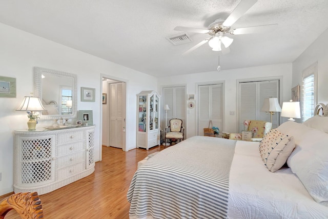 bedroom featuring a textured ceiling, ceiling fan, light hardwood / wood-style floors, and multiple closets