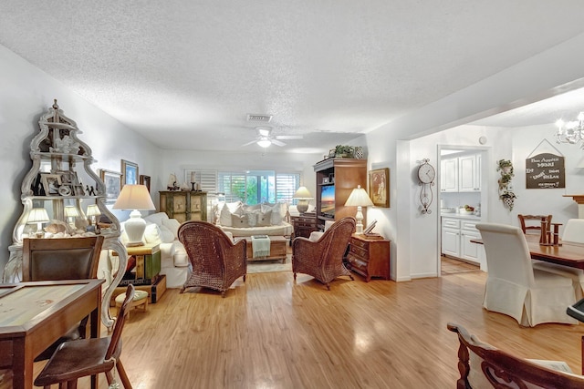 interior space with light wood finished floors, visible vents, ceiling fan with notable chandelier, and a textured ceiling