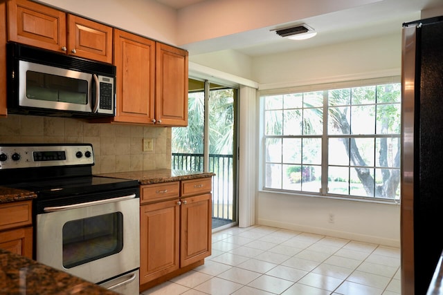 kitchen featuring dark stone counters, decorative backsplash, appliances with stainless steel finishes, and light tile patterned flooring