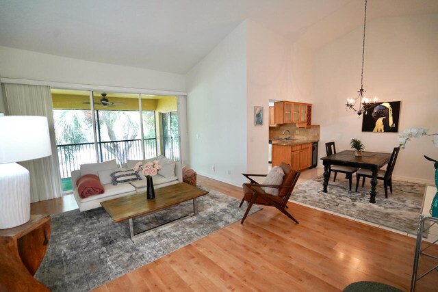 living room with light wood-type flooring, ceiling fan with notable chandelier, sink, and high vaulted ceiling