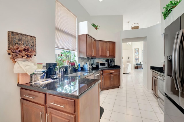 kitchen with dark stone counters, light tile patterned flooring, sink, stainless steel appliances, and backsplash