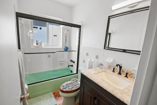 bathroom with vanity, tile walls, toilet, and shower / bath combination with glass door