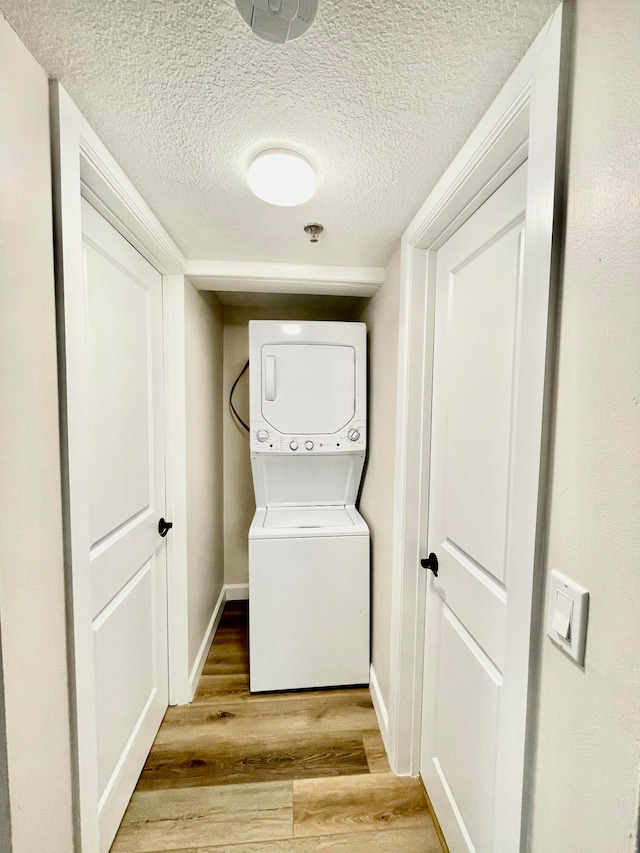 washroom featuring a textured ceiling, light hardwood / wood-style flooring, and stacked washer / dryer