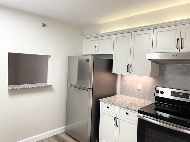 kitchen with white cabinetry, light hardwood / wood-style flooring, stainless steel appliances, light stone counters, and decorative backsplash