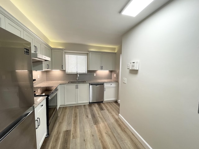 kitchen featuring light wood finished floors, backsplash, under cabinet range hood, appliances with stainless steel finishes, and a sink