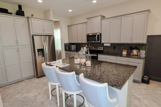 kitchen with a kitchen island, stainless steel appliances, dark stone countertops, light tile patterned flooring, and tasteful backsplash