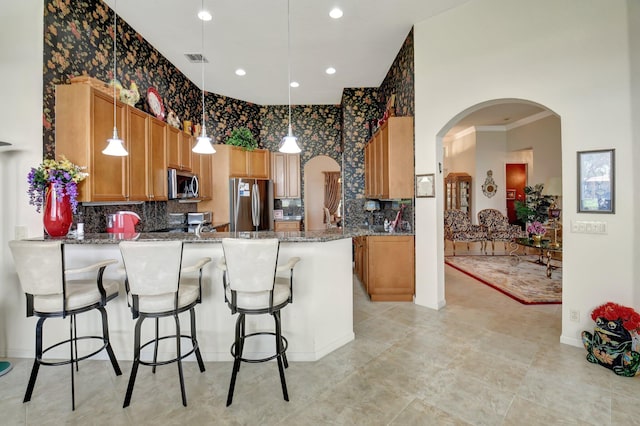 kitchen featuring crown molding, appliances with stainless steel finishes, dark stone counters, kitchen peninsula, and a breakfast bar