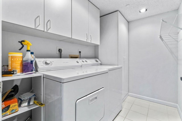 laundry room featuring a textured ceiling, cabinets, washer and clothes dryer, and light tile patterned floors