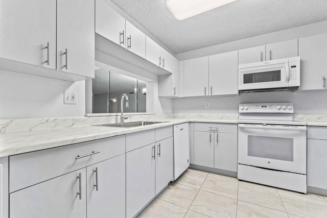 kitchen with a textured ceiling, light stone counters, sink, and white appliances