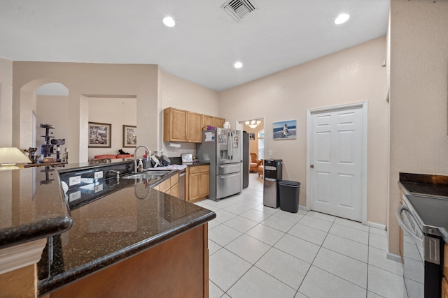 kitchen featuring dark stone counters, stainless steel appliances, light tile patterned floors, kitchen peninsula, and sink