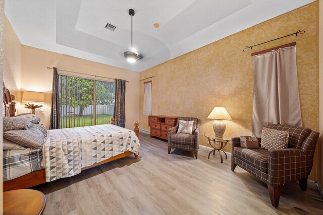 bedroom with a raised ceiling, light hardwood / wood-style flooring, and access to exterior