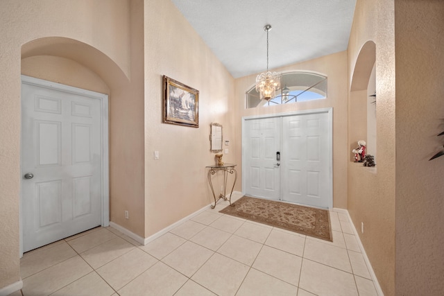 foyer entrance with a textured ceiling, an inviting chandelier, and light tile patterned flooring