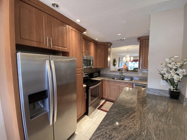 kitchen featuring dark stone countertops, a chandelier, light tile patterned floors, stainless steel appliances, and sink