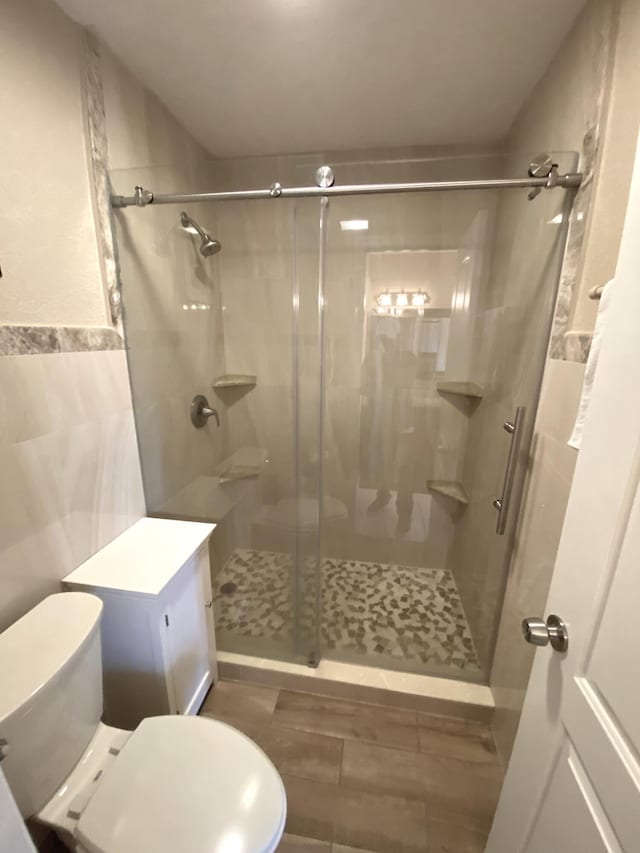 bathroom featuring toilet, hardwood / wood-style floors, a shower with door, vanity, and tile walls