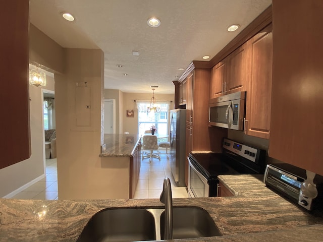 kitchen with pendant lighting, light tile patterned floors, light stone counters, sink, and appliances with stainless steel finishes