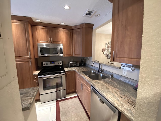 kitchen featuring a textured ceiling, light tile patterned floors, appliances with stainless steel finishes, sink, and dark stone countertops