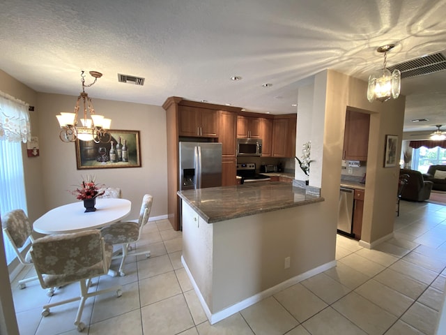 kitchen featuring light tile patterned floors, an inviting chandelier, stainless steel appliances, dark stone counters, and a textured ceiling