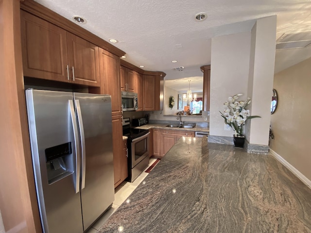 kitchen featuring an inviting chandelier, decorative light fixtures, stainless steel appliances, sink, and a textured ceiling