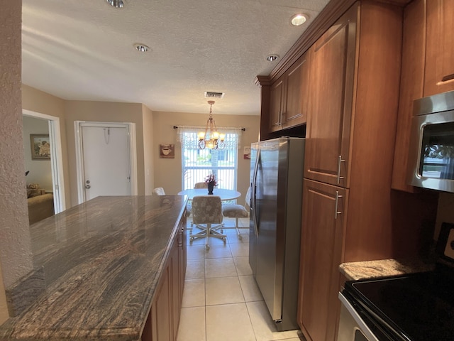 kitchen with a textured ceiling, an inviting chandelier, pendant lighting, light tile patterned floors, and appliances with stainless steel finishes