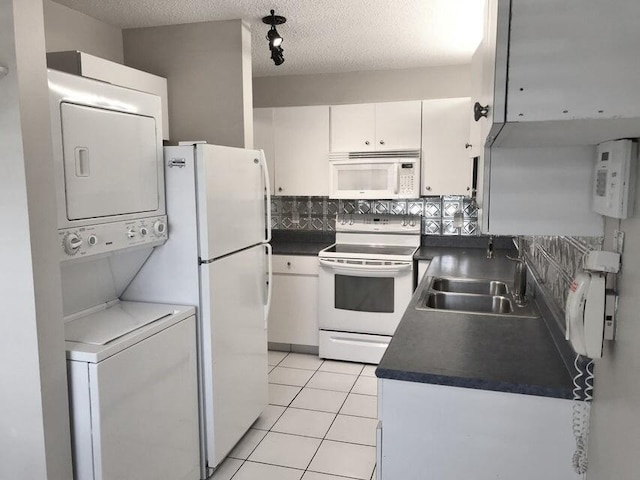 kitchen featuring sink, light tile patterned floors, white appliances, white cabinets, and stacked washer and clothes dryer