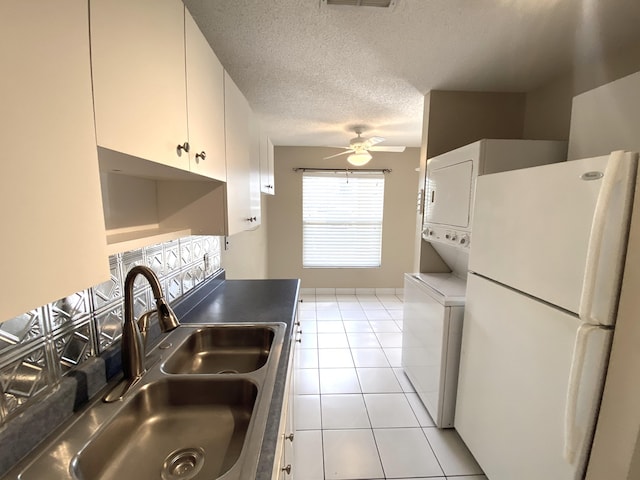 kitchen with white cabinets, sink, stacked washing maching and dryer, a textured ceiling, and white fridge