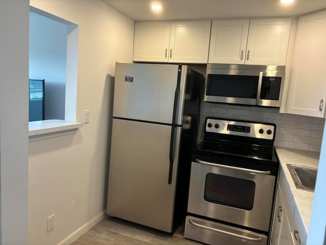 kitchen with backsplash, stainless steel appliances, white cabinetry, and light hardwood / wood-style flooring