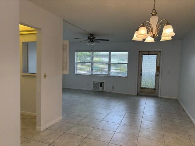 empty room with light tile patterned flooring, ceiling fan with notable chandelier, and a wall mounted AC