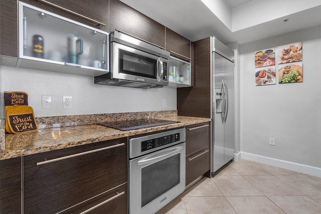 kitchen with dark brown cabinets, light tile patterned floors, dark stone counters, and appliances with stainless steel finishes