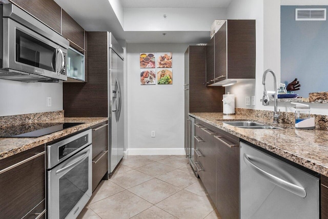 kitchen featuring dark brown cabinetry, sink, stainless steel appliances, light stone counters, and light tile patterned flooring