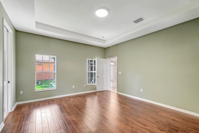 unfurnished room featuring a tray ceiling, a textured ceiling, and hardwood / wood-style flooring