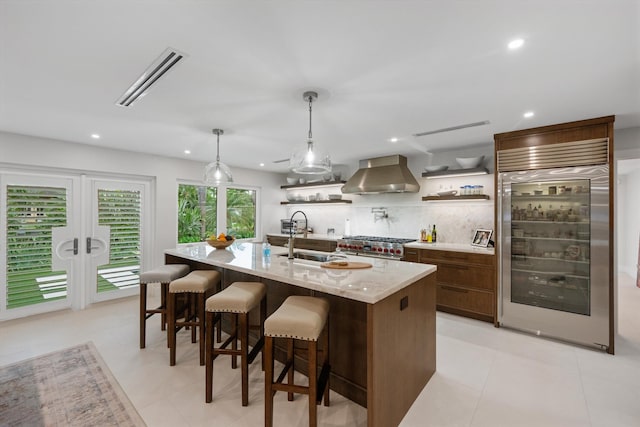 kitchen with wall chimney exhaust hood, an island with sink, a breakfast bar, decorative backsplash, and premium appliances