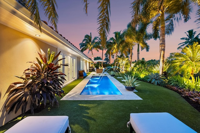 pool at dusk with a yard, a patio, and pool water feature