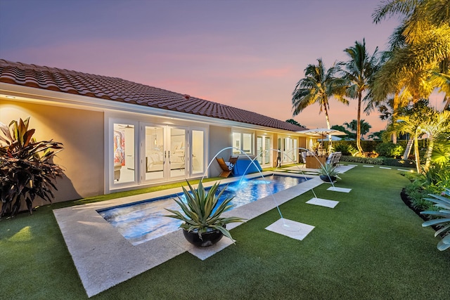 pool at dusk featuring a patio area, pool water feature, a yard, and french doors