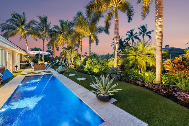 pool at dusk featuring a yard and pool water feature