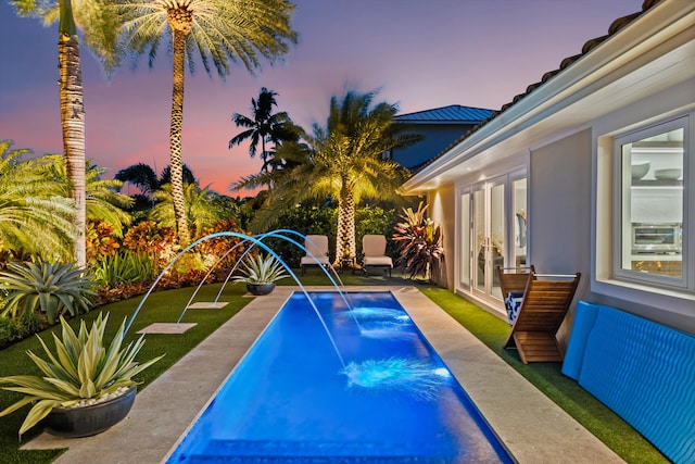 pool at dusk featuring pool water feature