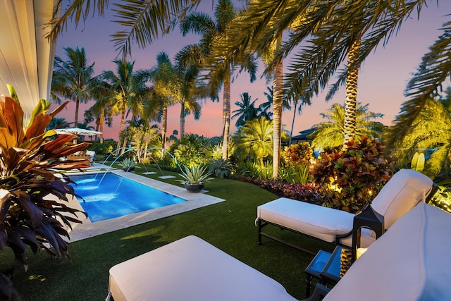 pool at dusk with a patio area, a lawn, and pool water feature