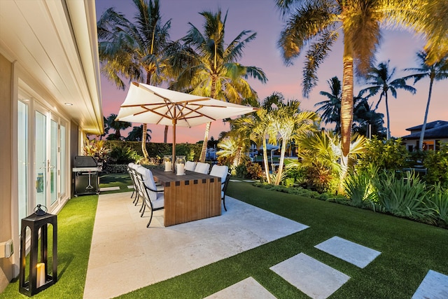 patio terrace at dusk with a lawn and area for grilling