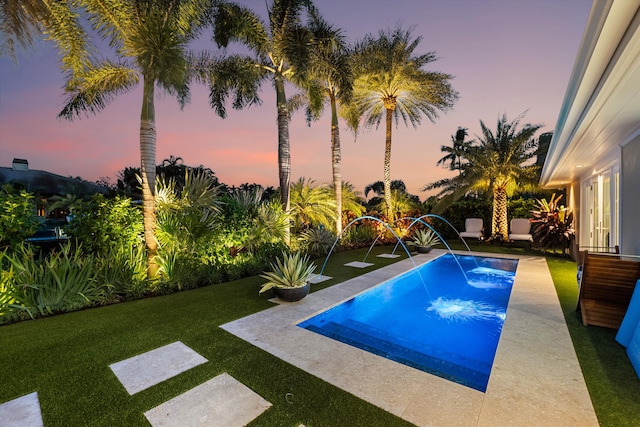 pool at dusk featuring a yard, pool water feature, and a patio area