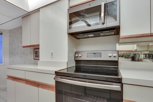 kitchen featuring a drop ceiling, light tile patterned floors, white cabinetry, and appliances with stainless steel finishes