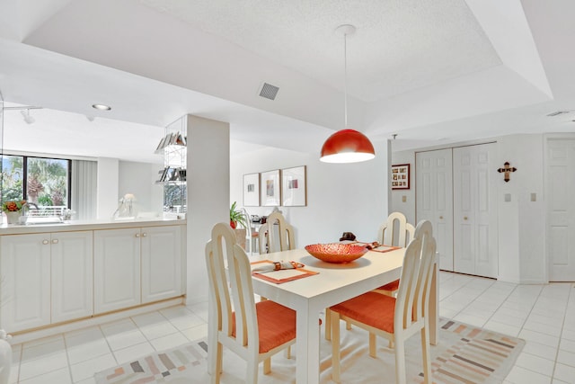 dining space with a raised ceiling, light tile patterned flooring, and a textured ceiling