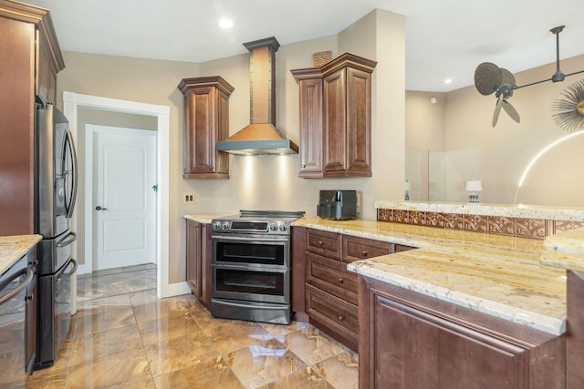 kitchen featuring kitchen peninsula, wall chimney range hood, stainless steel appliances, decorative columns, and light stone countertops