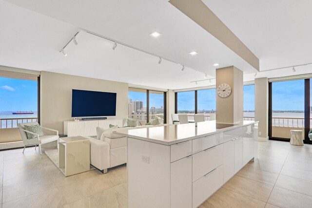 kitchen with a water view, a center island, white cabinets, track lighting, and light tile patterned flooring