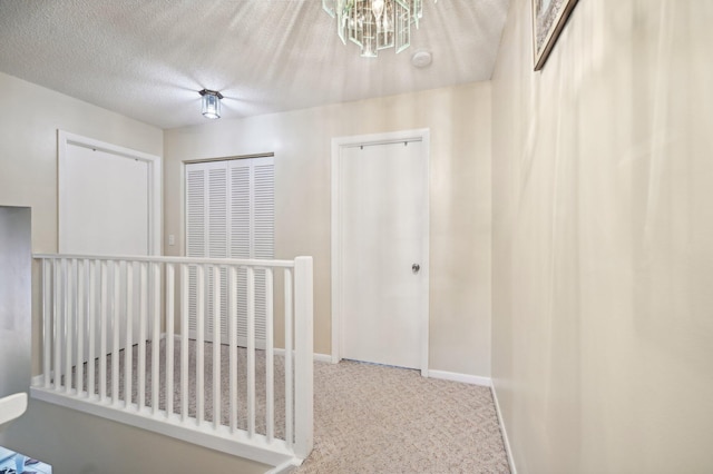 corridor with carpet flooring, a textured ceiling, and an inviting chandelier